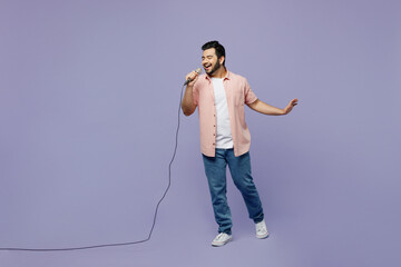 Wall Mural - Full body young Indian man he wear pink shirt white t-shirt casual clothes sing song in microphone at karaoke club isolated on plain pastel light purple background studio portrait. Lifestyle concept.