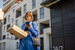 © rh2010 - Young woman using smart phone while standing with a parcel delivered with post office machine with automatic lockers. New technologies in delivery service, self picking