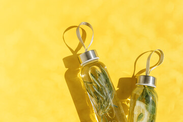 Wall Mural - Top view two glass bottles, water drink detox with lemon and mint leaves, and rosemary, at sunlight on yellow background, Infused water, wellness trend. Aesthetic Refreshing summer drink