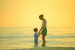 © grooveriderz - Happy family resting at beach in summer, Mother and baby boy feet at the sea foam at the sunlight water is moving