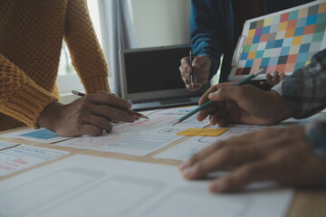 Close up ux developer and ui designer brainstorming about mobile app interface wireframe design on table with customer breif and color code at modern office.Creative digital development agency