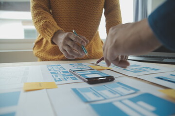 Close up ux developer and ui designer brainstorming about mobile app interface wireframe design on table with customer breif and color code at modern office.Creative digital development agency