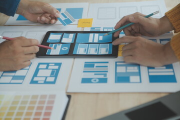 Close up ux developer and ui designer brainstorming about mobile app interface wireframe design on table with customer breif and color code at modern office.Creative digital development agency