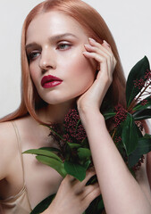 Wall Mural - Beautiful young fair-skinned woman with red hair posing in the studio on a white background. Red flower in the hands. Skin and hair care. Natural cosmetics, spa, beauty salon. Care cosmetics.