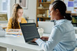 © AnnaStills - Young woman typing codes on laptop while sitting at table with her colleague in office