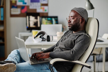 african american developer working with software on laptop while sitting on chair in office