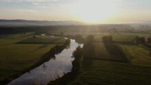 A Slow And Sleepy River With Mist In The Green Countryside At Sunrise