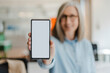 © Maria Vitkovska - Smiling confident senior woman holding mobile phone, showing digital screen, mockup. Happy 60 years old, gray haired female using modern mobile app shopping online, selective focus. Technology