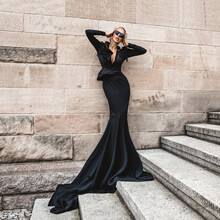 Elegant Luxury Evening Fashion. Glamour, Stylish Elegant Woman In Black Long Evening Gown Dress Is Posing In The City Outdoor. Female Model In Amazing Long Dress. Outdoor Shoot. Vogue. Couture.
