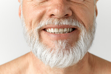 Cropped close-up image of grey-haired man's beard. Mature male model smiling against grey background. Dental teeth care. Concept of male beauty, face and skin care, daily procedures, age