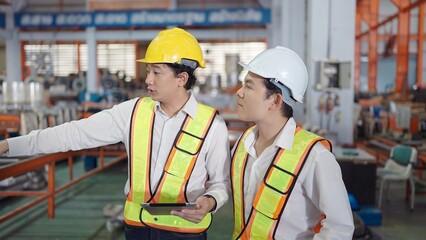 Wall Mural - Two professional asian engineers men in safety uniform holding tablet working and discuss while walking at industrial factory. Manufacturing industry concept