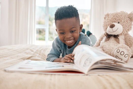Young african boy, reading and bed for story, book and learning with smile in family home, focus and excited. Black male child, education and relax in bedroom with happiness, study or comic in house