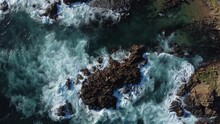 Aerial drone view of foamy waves breaking on a rocky shore