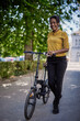 © kerkezz - Young woman pushing bicycle in park, looking at camera and smiling.