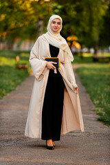 Wall Mural - Full length portrait of a beautiful Muslim woman wearing elegant modern fashion hijab outside.