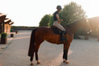 professional horsewoman on her horse outside stables in the warm light of the evening