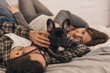 Happy couple is having fun and playing with their French Bulldog puppy lying on the bed at home.Family and animal life concept.