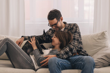 Happy couple is having fun and playing with their French Bulldog puppy at home.Family and animal life concept.