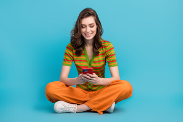 Poster - Full size photo of positive woman dressed orange pants colorful cardigan look at smartphone read email isolated on blue color background