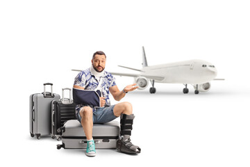 Canvas Print - Disappointed male tourist with an injured arm and leg sitting on suitcases and waiting for a plane