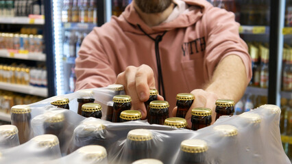 An opened pack of beer bottles in alcohol department and a buyer takes two of them