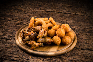 Wall Mural - Snack breaded mozzarella cheese balls, crispy squid rings breaded (caramari) and chicken legs on wooden board.