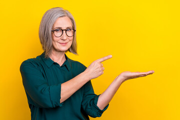 Portrait of elegant lady indicate finger hand hold empty space wear green isolated on yellow color background