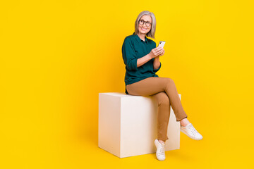 Sticker - Full length portrait of nice cheerful aged persons sit podium use smart phone look empty space isolated on yellow color background