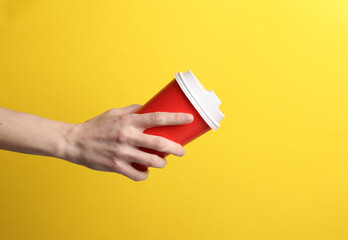 Wall Mural - Hand holding red disposable take out cup for hot drinks mockup (tea, coffee) on yellow background