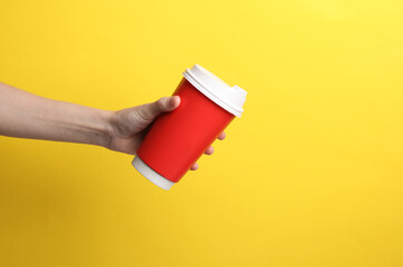 Hand holding red disposable take out cup for hot drinks mockup (tea, coffee) on yellow background