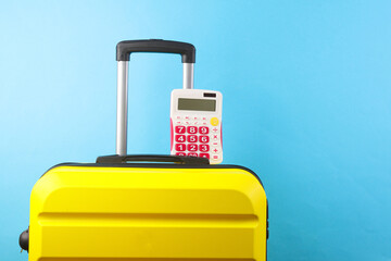 Yellow plastic travel suitcase with calculator on blue background. Holiday budget