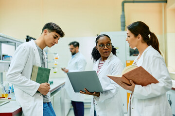 Wall Mural - Black scientist and her coworkers talk while working on laptop in laboratory.