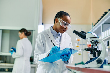 Wall Mural - african american biotechnologist writing data during scientific research in laboratory.