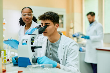 Wall Mural - young biochemist looking through microscope during research in lab.