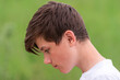  cute Teenage boy in profile is looking down green natural background nature park.