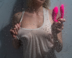 A woman in a white tank top stands in the shower and holds a curved pink sex toy. 