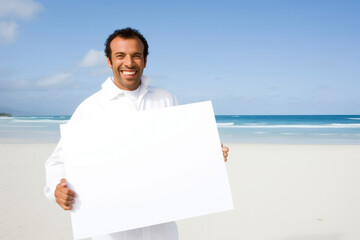 Poster - Portrait of a smiling man holding a blank sheet of paper on the beach