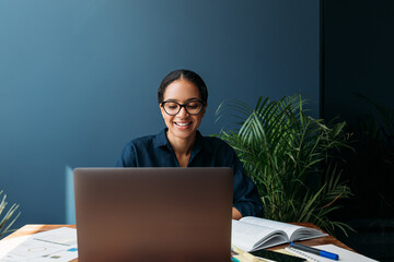 Cheerful woman in eyeglasses at the table working on laptop at home