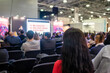 © zyabich - Business, congress, seminar, corporate, training, education concept. Back view of woman in red dress and unrecognizable people, audience listening lecture, presentation at trade show, conference hall
