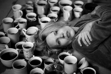 Wall Mural - Woman surrounded by many cups of coffee, deadline concept. Workaholism, overtime, the need to be alert. Tired woman. Black and white photo.