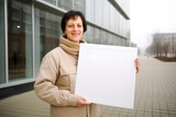 Fototapeta  - Mature woman holding a whiteboard in her hands on the street