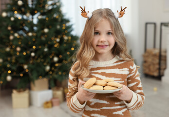 Canvas Print - Portrait of cute little girl in Christmas hair clips holding plate with cookies at home