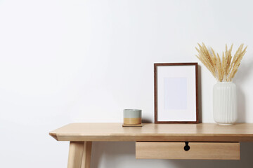 Wall Mural - Empty photo frame, cup and vase with dry decorative spikes on wooden table. Mockup for design