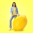 canvas print picture - Happy young woman with big lemon on yellow background