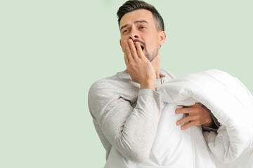 Wall Mural - Handsome man with soft blanket yawning on green background