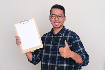 Asian man smiling and give thumb up while holding empty paper on clipboard