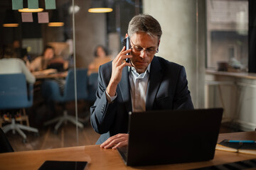 Businessman in office. Handsome man talking on phone at work..