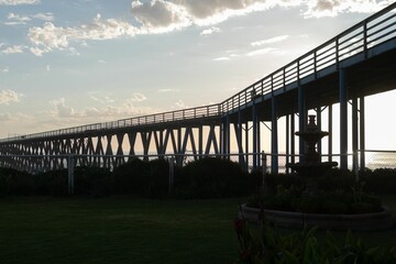 Sticker - Backlight shot of a long pier over the water and green feilds at sunset