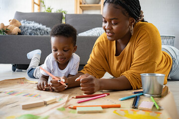 cheerful african-american mother and cute toddler son playing with colored pencils, drawing on a big