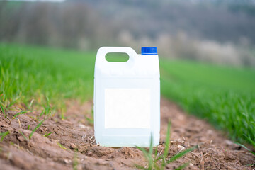 Wall Mural - white plastic container with agricultural chemicals or fertilizers on a green field